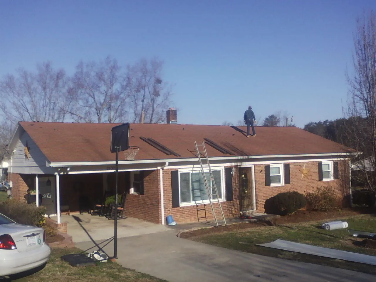 Roofer stripping a shingle roof on a brick ranch before metal panels in Peck