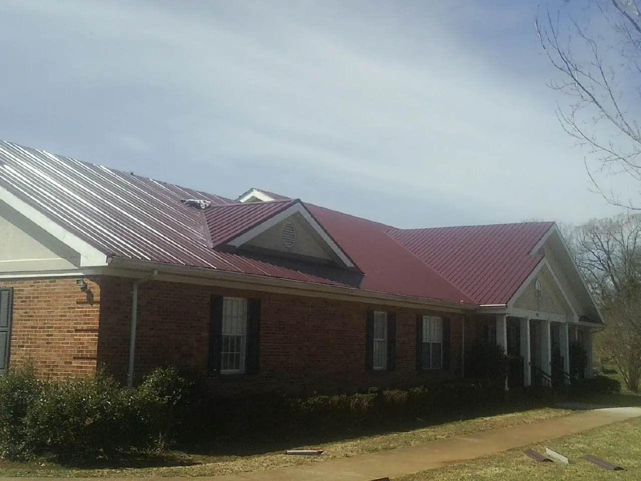 Red metal roof with gabled entries on a long brick building, from a Hail Damage Roof Repair job in Peck