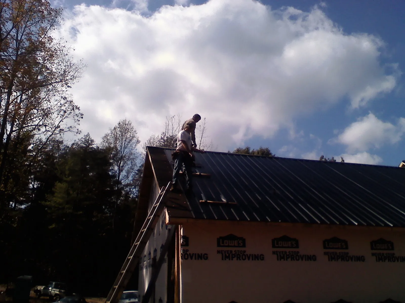 Roofer fastening dark metal panels high against a cloudy sky, from a Roof Inspection job in Peck