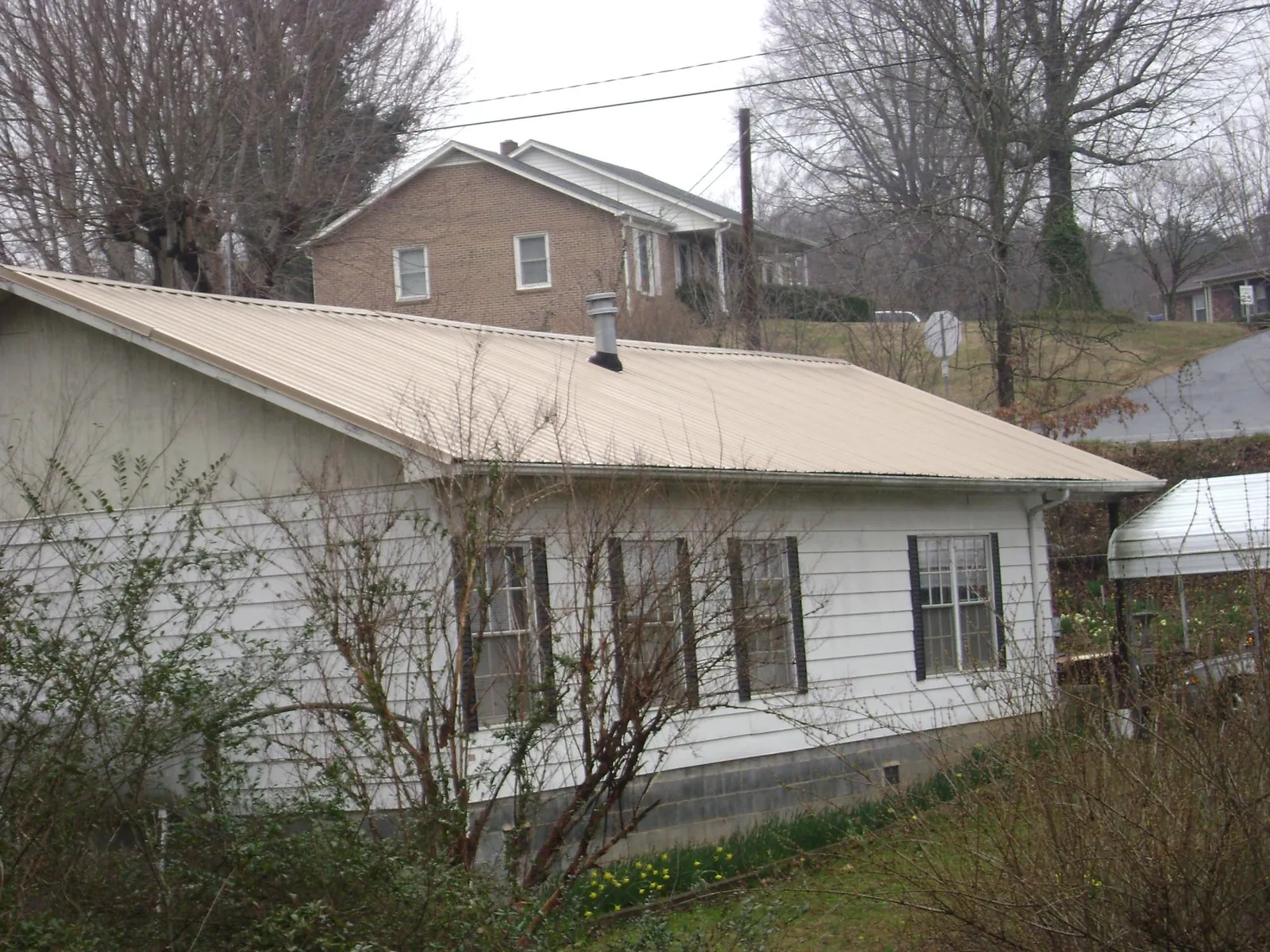 Tan metal roof on a white sided house set into a hillside — Commercial Roofing by Roofing Brothers in Peck